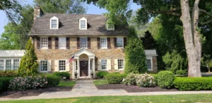 Two-story stone house with a front porch, surrounded by landscaped gardens.
